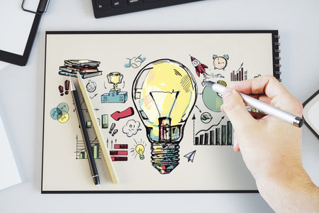 Close up of hand drawing creative light bulb sketch on desk. Idea, innovation and creativity concept