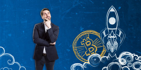 A man in a suit contemplating with hand-drawn illustrations of a Bitcoin and a rocket on a blue textured background, concept of a cryptocurrency startupの写真素材