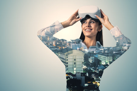 A woman wearing virtual reality goggles, with a cityscape superimposed, against a plain background,...