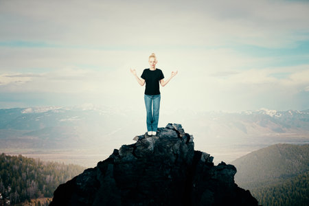 Attractive young woman standing on mountain top and meditating. Bright sky background with mock up...