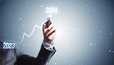 A person in a suit drawing an ascending arrow from 2023 to 2024, indicating growth or progress on a...
