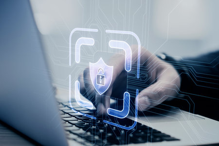 A person working on a laptop with a digital security hologram concept overlay on a blurred...