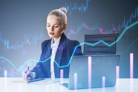 A businesswoman analyzing financial graphs overlaid on the image, with a laptop and notebook, on a light digital background, concept of market analysisの写真素材
