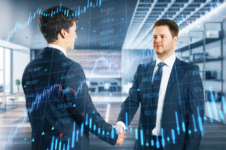 Two attractive young European men shaking hands in bright office interior with forex chart....