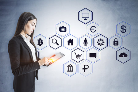 Attractive young businesswoman using tablet with creative hexagonal pattern business sketch on concrete wall background. Success, technology and finance conceptの写真素材