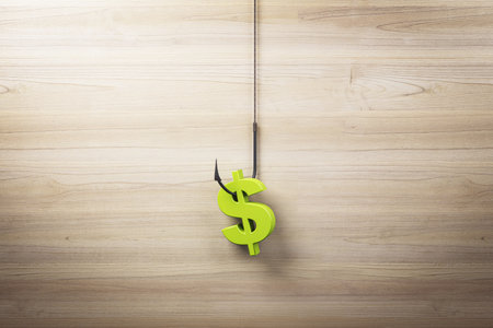A green dollar sign on a fish hook hangs against a wooden background. Represents concepts of...