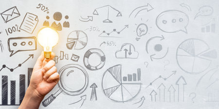 A hand holding a bright lightbulb against a backdrop of various business sketches and charts on a whiteboard. Concept of creative ideas and business strategyの写真素材