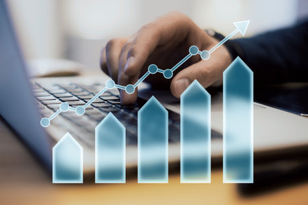 Closeup of a hand typing on a laptop, with a transparent arrow and bar chart overlay on a blurred background. Concept of business growth and financial successの写真素材