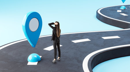 Woman in a black suit stands on a winding road with a large blue location pin, representing navigation and decision-making. Sky blue background. Concept of finding directionの写真素材