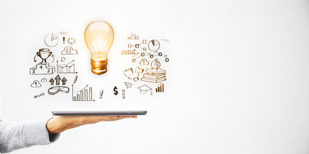 Hand holding tablet with a glowing lightbulb and business sketches on a white background. Concept of innovation, ideas, and strategyの写真素材