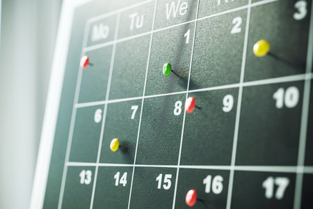 Close-up view of a calendar with colorful pins marking important dates. Dark green background. Concept of scheduling and planning. 3D Renderingの写真素材