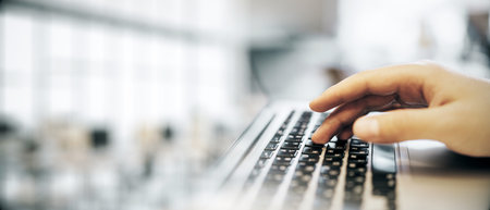 Closeup of a person's hand typing on a laptop keyboard in a bright, blurred office background. Concept of business, work, and technologyの写真素材