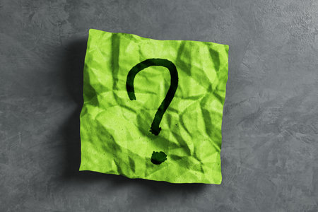 Green crumpled paper with a black question mark on a grey textured background. Concept of...