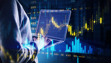 Person using a laptop to analyze forex trading data with virtual financial graphs overlayed on a blue digital background, indicating growthの写真素材