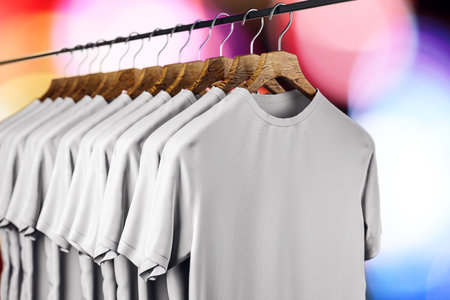 Row of empty white t-shirts hanging on rack on blurry bokeh background. Mock up place. Fashion and showroom concept. 3D Renderingの写真素材