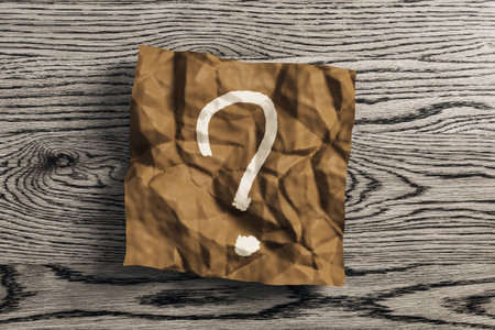 Close up of wrinkled brown piece of paper with question mark on wooden desk background. Supplies, stationery, school, work and education concept. 3D Renderingの写真素材