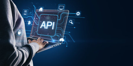 A person working on a laptop, showing API icons and network symbols, glowing in blue. Holographic...