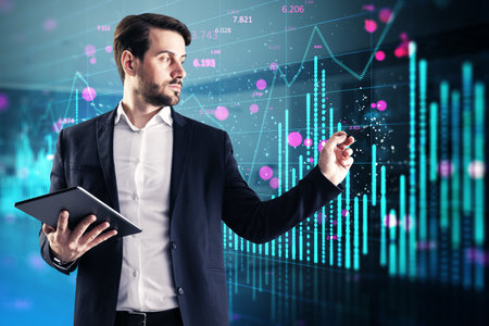 Attractive young caucasian businessman using tablet with glowing blue forex chart on blurry office interior background. Financial growth, trade and stock conceptの写真素材
