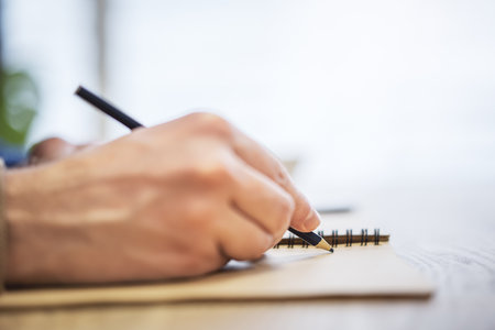 Close perspective of a man's hand making entries in a notepad, with a soft blur in the surroundingの写真素材