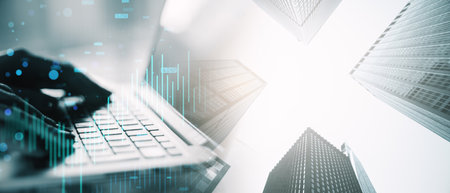 Hands typing on a laptop with financial charts and skyscrapers in a double exposure style. Concept...