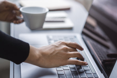 Picture focuses on a woman's hands typing on a contemporary laptop keyboard, office setting...