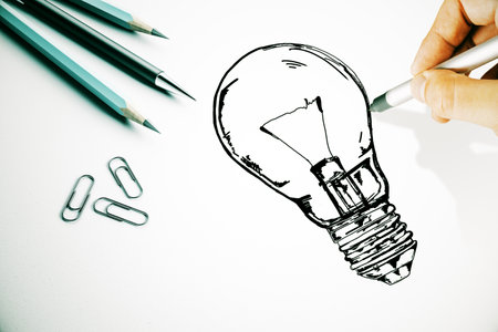 Hand drawing of a lightbulb next to pencils and paper clips on a white background. The image represents creativity, innovation, and brainstormingの写真素材