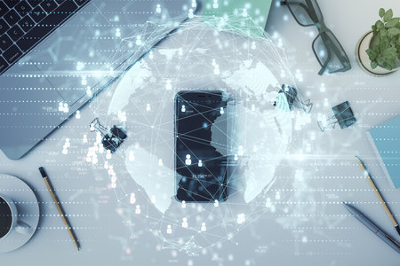 Abstract digital globe network overlaying a desk with laptop, phone, and office items, symbolizing modern global connectivityの写真素材