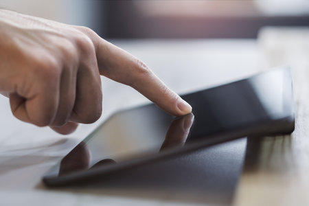 Closeup view of a male finger operating a high-tech tablet on a desk, set against the blurred...