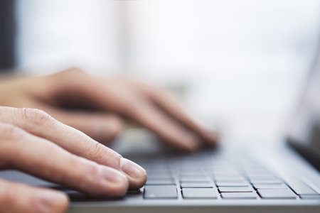 The image presents a man's hands up close as they navigate a modern laptop's keyboard, against a...