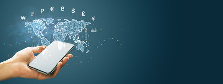 A hand holds a smartphone with a holographic world map, currency symbols, and graphs on a blue...