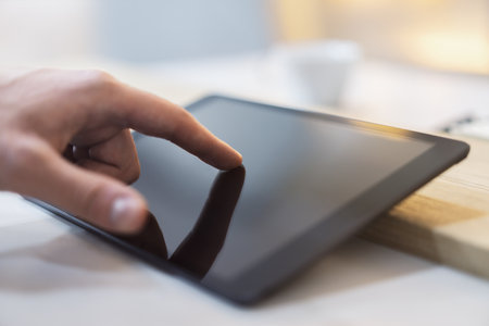Close detail of a man's finger making contact with the screen of a sleek digital tablet resting on a...
