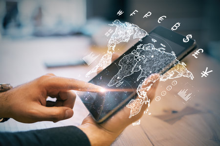 Hands using a smartphone with holographic icons and world map, modern digital interface, wooden desk background, concept of global financeの写真素材