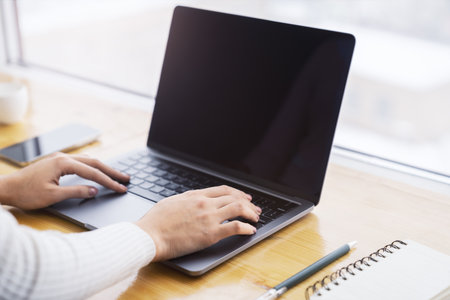A close-up view of female hands typing on a state-of-the-art laptop keyboard, with a blurry office setting behindの写真素材