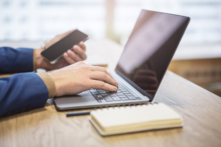 Against a blurry office backdrop, a man's hands are seen in close detail, typing on a trendy laptop...