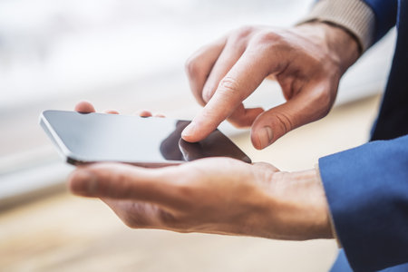 Man engaged with his modern smartphone out of focus nearby against the blurred office hustle and bustleの写真素材