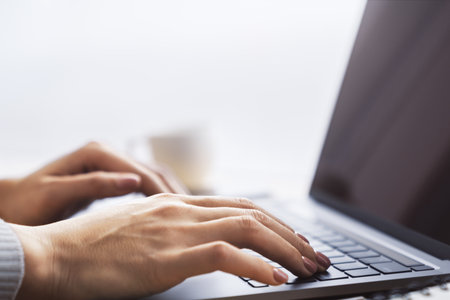 Against a blurred office scene, a close-up shot reveals a woman's hands typing on a modern laptop...