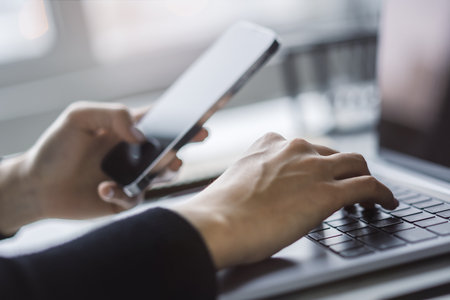 Set against a fuzzy office backdrop, the image presents a woman's hands typing on a modern laptop keyboardの写真素材