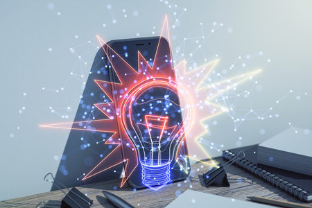 Abstract holographic light bulb over smartphone on desk with stationery items, glowing lines and nodes, concept of innovation and technologyの写真素材