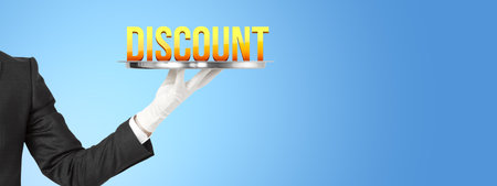 A person in a suit with a white glove holds a silver tray with the word DISCOUNT on it against a blue background, symbolizing a sale conceptの写真素材