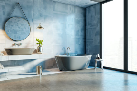 Stylish bathroom with freestanding tub, round mirror, and blue wall tiles, illuminated by sunlight...