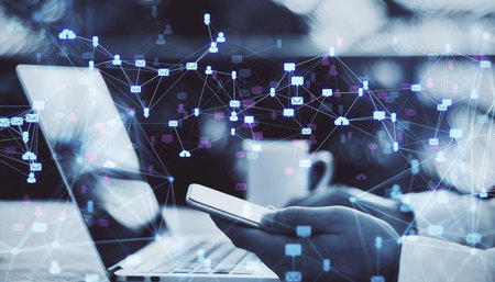 Person using smartphone and laptop with digital social media icons overlay on blurred office...