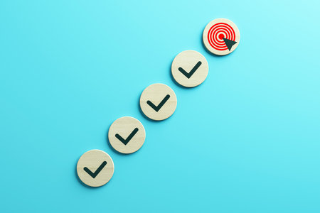 Wooden circles with check marks and a target icon arranged diagonally on a light blue background, representing steps to achieving goals. 3D Renderingの写真素材