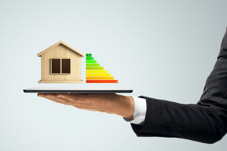 Wooden house model and energy rating chart floating above tablet held by man in suit on light background, concept of smart home and property efficiencyの写真素材