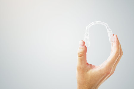 Hand showing clear dental aligner on clean gradient background, concept of modern orthodontic treatment and dental technology presentationの写真素材