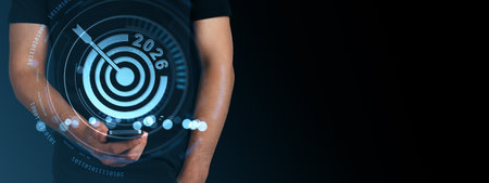 Person holding phone with futuristic digital target and 2026 text, glowing interface on dark background, concept of goal setting and innovationの写真素材