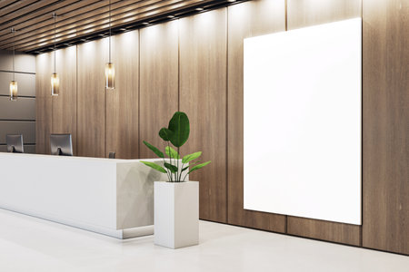 Modern reception room with a blank vertical canvas on a wooden wall, clean white counter desk, ceiling lights, and plant decor. 3D Renderingの写真素材