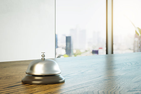 Hotel reception bell on wooden desk, realistic style, with bright blurred city background. Concept of hospitality, service, and welcome. 3D Renderingの写真素材