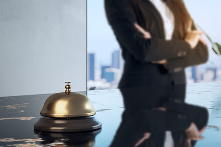 Golden service bell on glossy hotel reception counter with blurred businesswoman in suit in background, modern interior, hospitality conceptの写真素材