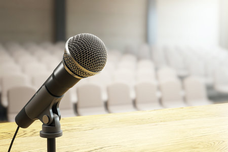 Microphone closeup on wooden stage podium with blurred auditorium chairs in background, light scene background concept of speech or conference. 3D Renderingの写真素材