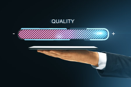 Businessman hand holding tablet with glowing quality progress bar above, modern digital interface on dark background, concept of improvementの写真素材
